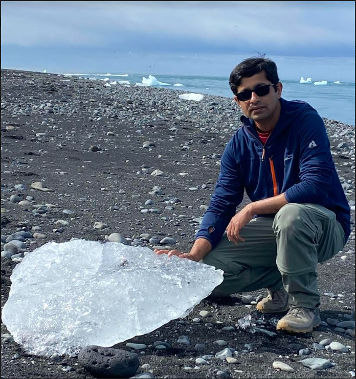 Ambarish Karmalkar holding small piece of ice on rocky waterfront.